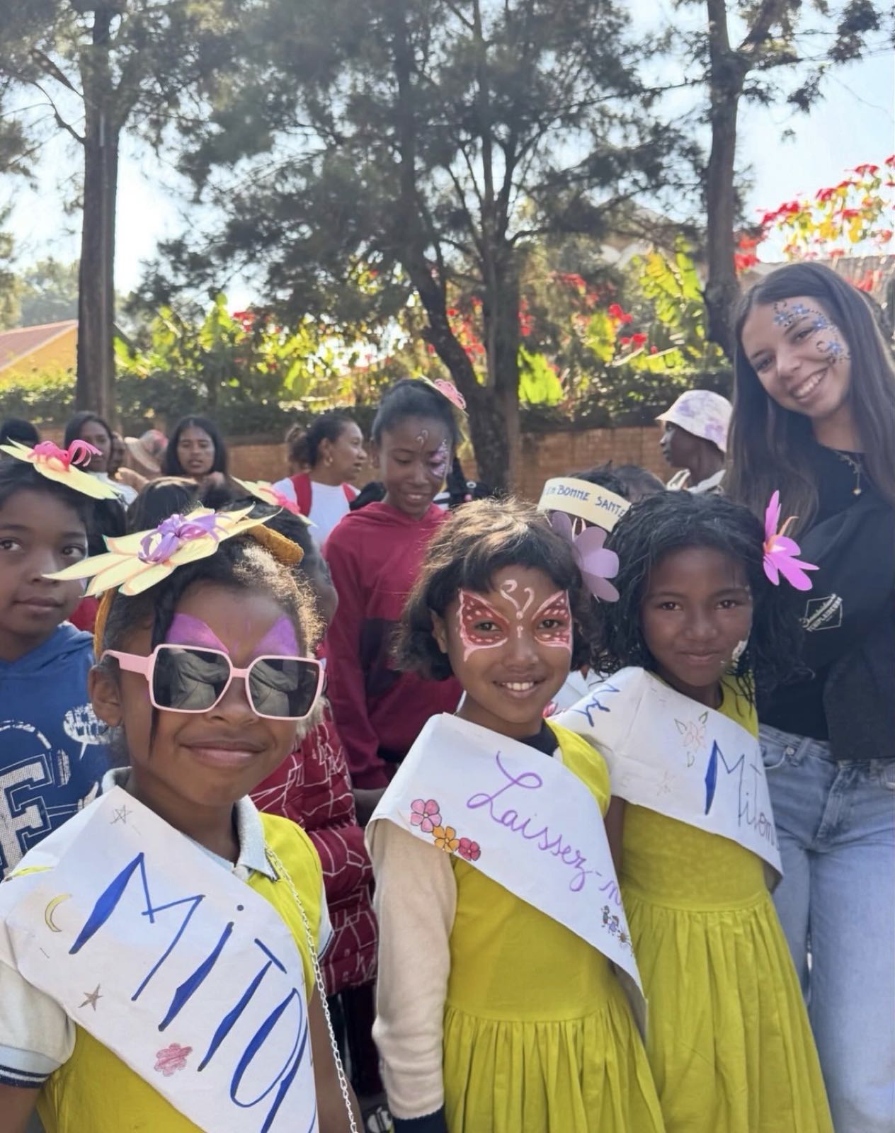 Des enfants en robe jaune et une bénévole souriante, visages maquillés, lors d'une fête à Madagascar