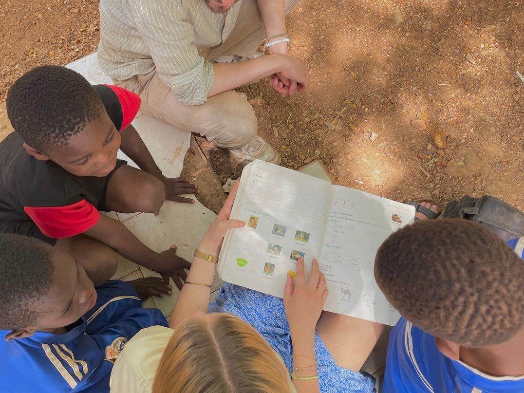 Une bénévole lit un manuel scolaire avec des enfants assis par terre au Sénégal