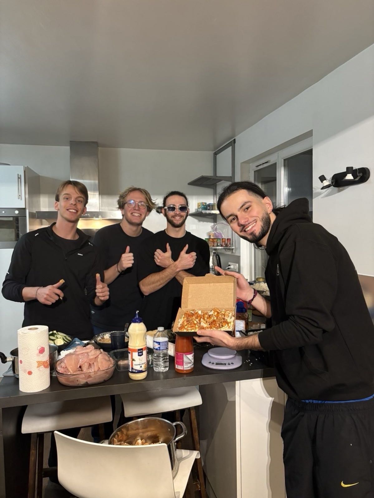 Quatre membres de l'asso en cuisine, pouces levés, présentent une box de tasty crousty